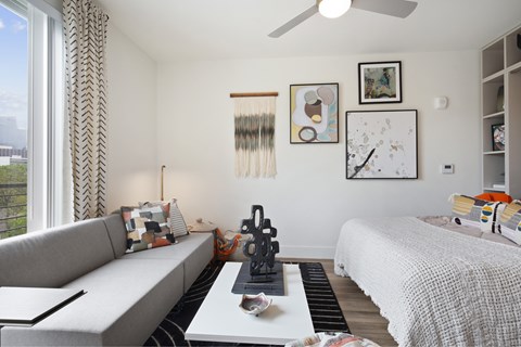 A living room with a grey couch and a white bed.