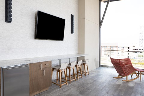 A modern kitchen with a refrigerator, a counter, a TV, and a chair.