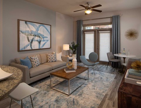 A living room with a grey couch, a coffee table, a chair, a table with a vase and a painting on the wall.