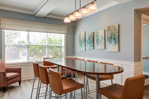 Resident lounge with high-top, oval-shaped table surrounded by stools with chair backs in front of an oversized window at Summit Place apartments in Methuen, MA.