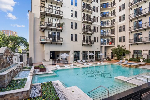A large swimming pool surrounded by a stone wall and a patio area with chairs and umbrellas.