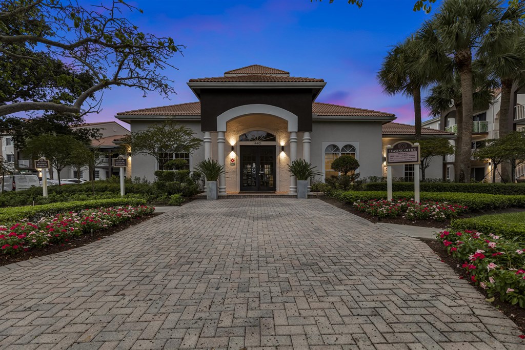 the front entrance of a villa with a brick walkway and palm trees