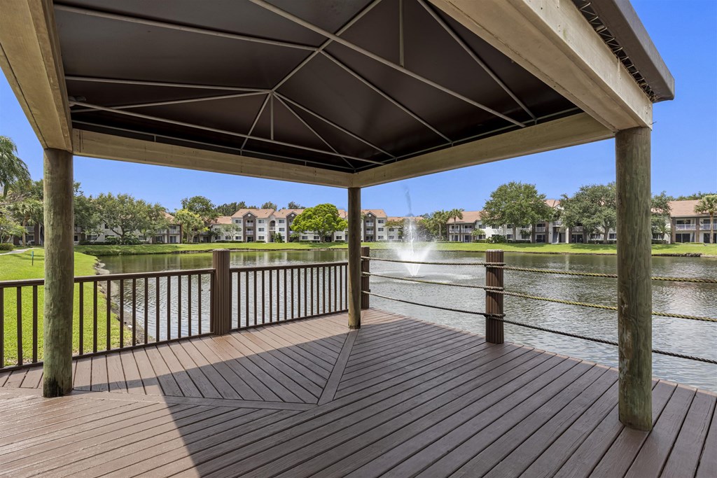 Covered deck area  with table and chairs overlooking community lake area with fountain feature