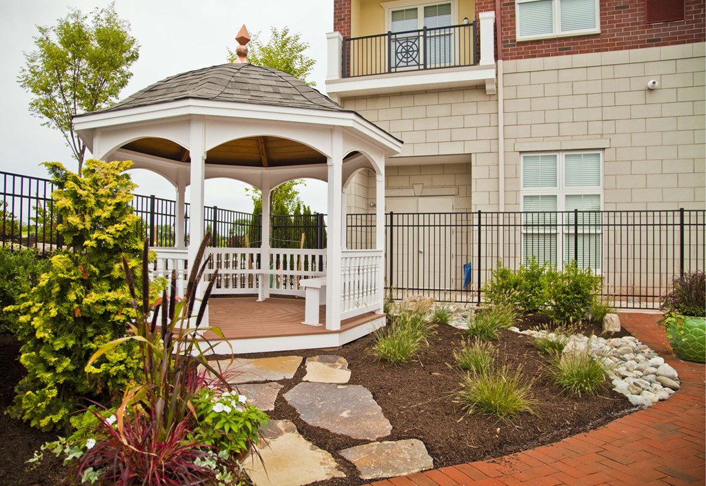 A gazebo is surrounded by a garden and a black fence.