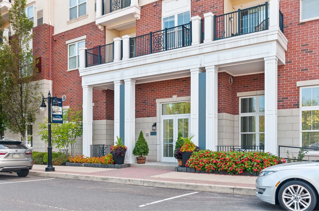 A red brick building with a white balcony and a white car parked in front.