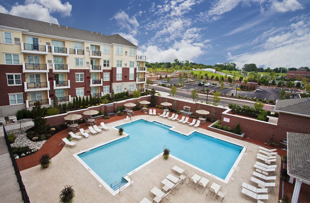 A large swimming pool surrounded by lounge chairs and apartment buildings.