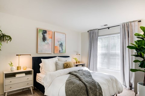 A bedroom with a large bed, a nightstand with a lamp, and a painting on the wall.
