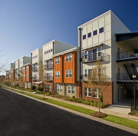 A row of modern apartment buildings with balconies and trees in front.
