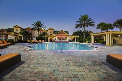 A pool surrounded by palm trees and a building in the background.