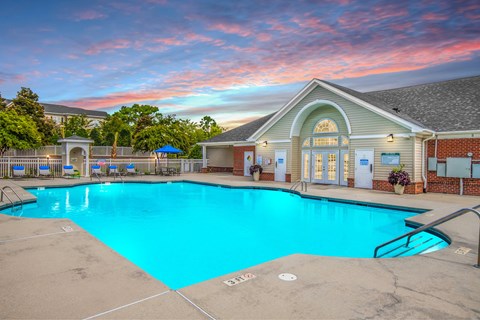 Wilmington, NC, Apartments With In-Unit Washer and Dryer - Bellingham Park - Swimming Pool With Metal Handrails, Concrete Decking, Lounge Chairs, And A Clubhouse Building.