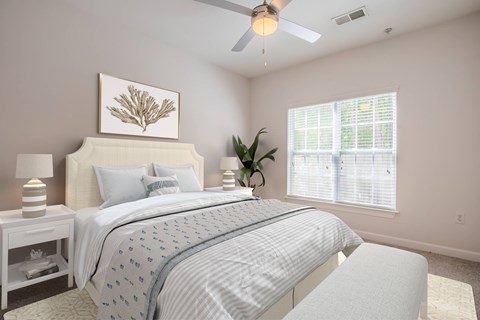 Three-Bedroom Apartments in Wilmington, NC - Bellingham Park - Bedroom With Lamps, Ceiling Fan, A Large Window, and Wall Art.
