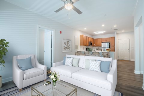 Pet-Friendly Apartments in Wilmington, NC - Bellingham Park - Living Room With White Sofa, Armchair, Glass Coffee Table, And a Ceiling Fan.