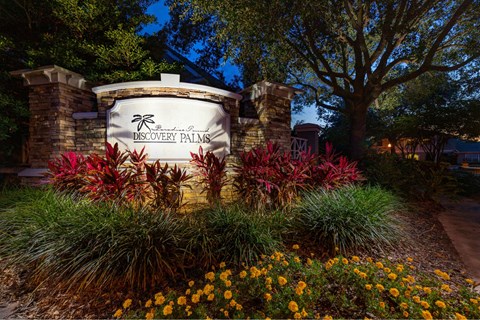 A sign for Discovery Palms is surrounded by flowers and plants.