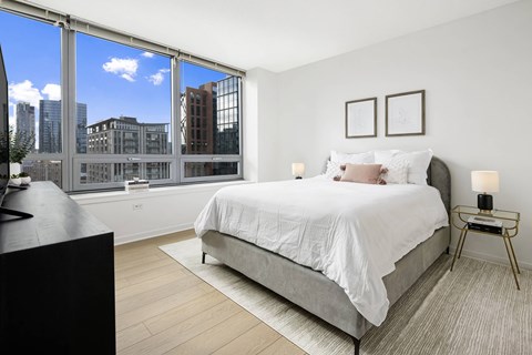 A bedroom with a large bed and a city view through the window.