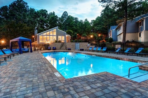 A swimming pool surrounded by a brick patio and lounge chairs.
