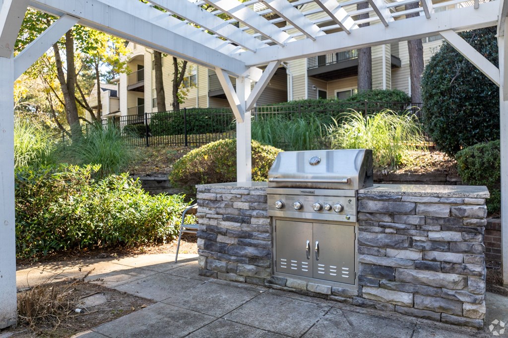 A BBQ grill is built into a stone wall under a white pergola.