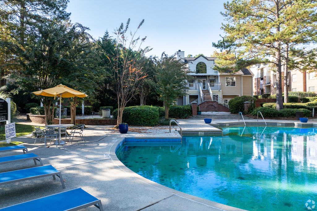 A pool with a yellow umbrella and blue loungers.