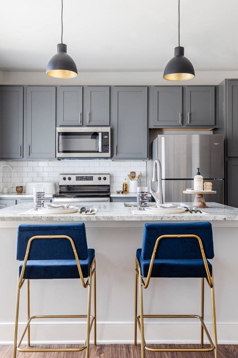 Two blue chairs with gold legs are in front of a kitchen island.