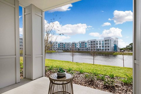 A balcony with a table and chairs overlooking a body of water and buildings.