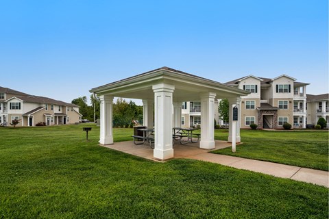 A white gazebo is in the middle of a grassy area with houses in the background.