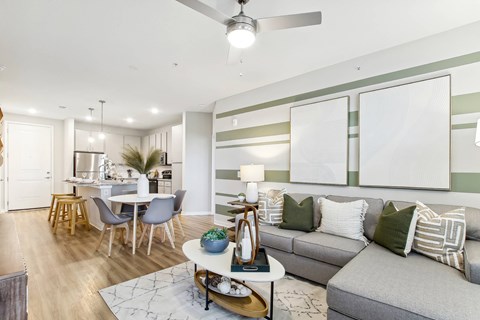 A modern living room with a grey sofa, a dining table with chairs, and a ceiling fan.