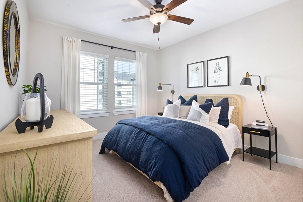 A bedroom with a bed, a ceiling fan, and a plant on a dresser.