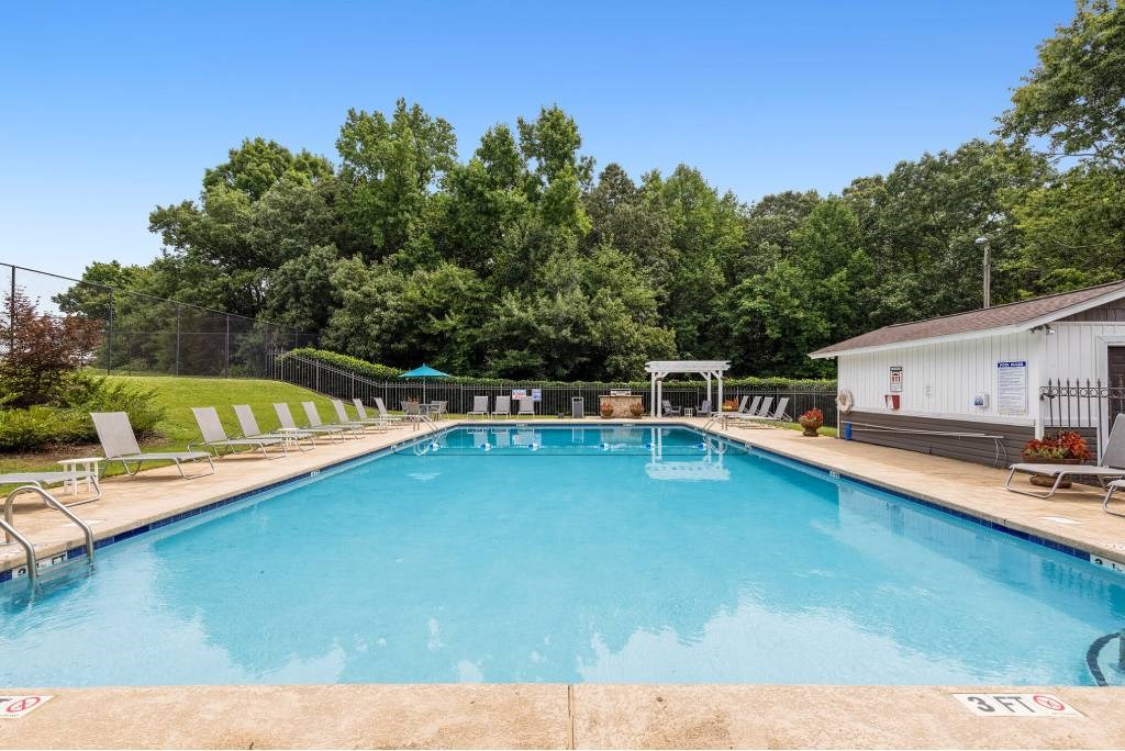 A large outdoor swimming pool surrounded by trees and lounge chairs.