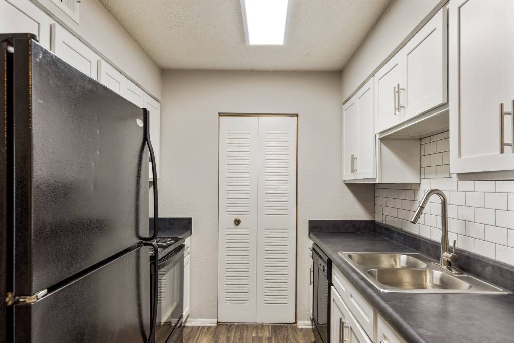 A black fridge sits in a kitchen with white cabinets and a white door.