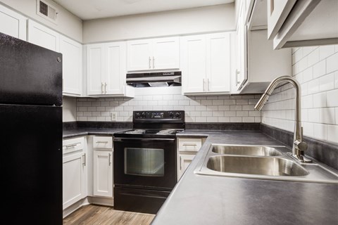 A black refrigerator sits next to a stove in a kitchen with white cabinets.