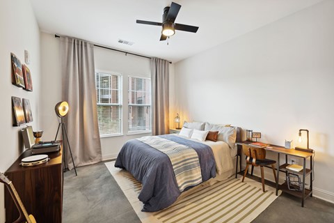 A bedroom with a bed, desk, chair, and a ceiling fan.