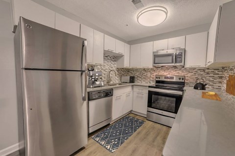 A kitchen with a stainless steel refrigerator and a stone backsplash.