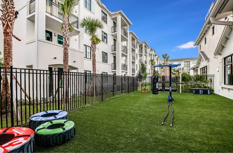A playground with a swing set in the middle of a grassy area in front of apartment buildings.