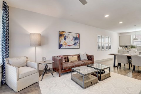 A modern living room with a white sofa, a glass coffee table, and a painting on the wall.