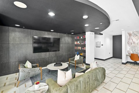 A modern living room with a grey couch, a coffee table, and a television on the wall.