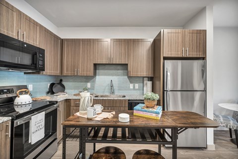 A kitchen with a black stove top oven and a black microwave above a counter with a wooden table and chairs.