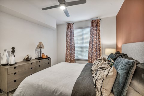 A bedroom with a bed, pillows, a ceiling fan, and a dresser with decorative items.