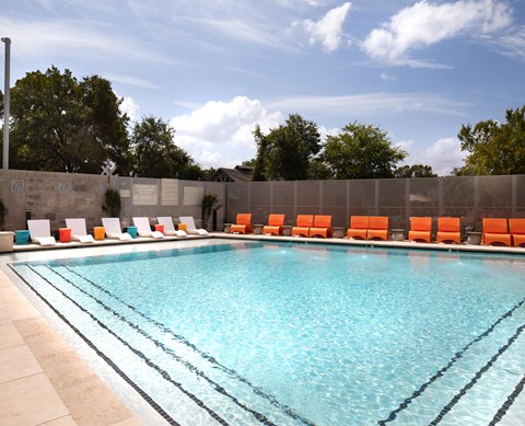 A swimming pool with orange chairs and a concrete wall.
