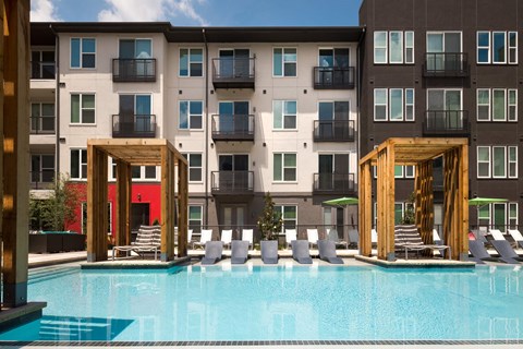 A pool area with lounge chairs and wooden structures in front of apartment buildings.