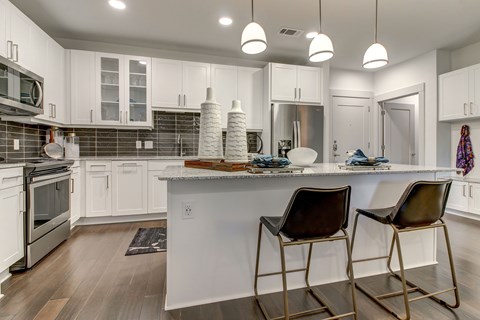 A kitchen with white cabinets and a white island with two chairs.