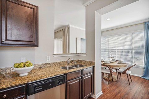 A kitchen with a black dishwasher and brown cabinets.