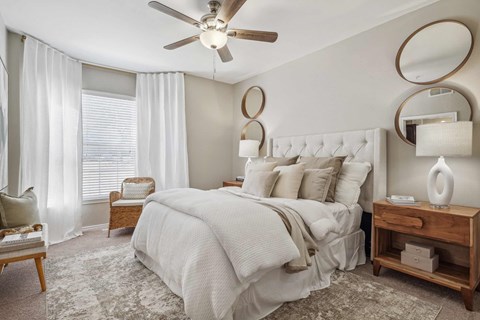 A bedroom with a large bed, a ceiling fan, and a nightstand with a lamp.