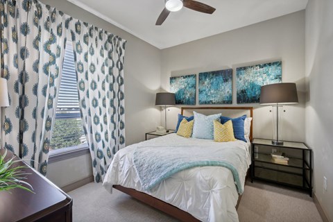 A bedroom with a bed, nightstand, and window with curtains.