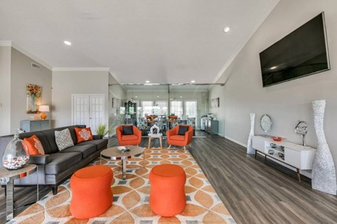 A living room with a grey couch, orange ottoman, and a television mounted on the wall.