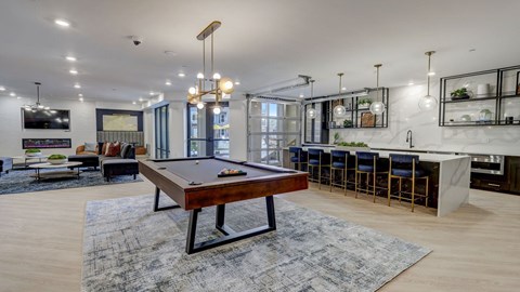A pool table is in the middle of a room with a bar and a kitchen in the background.