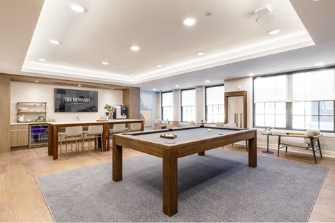 A billiard table is in the middle of a room with a kitchen area in the background.