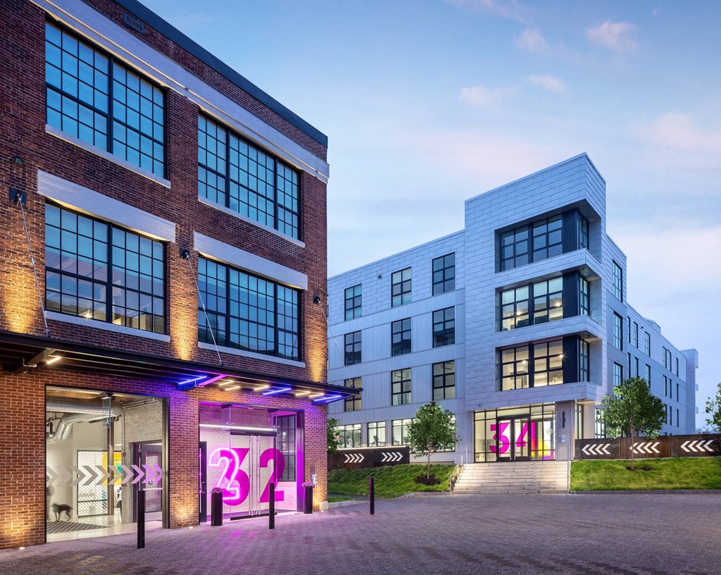A modern building with a glass facade and a brick exterior is illuminated with purple lighting.