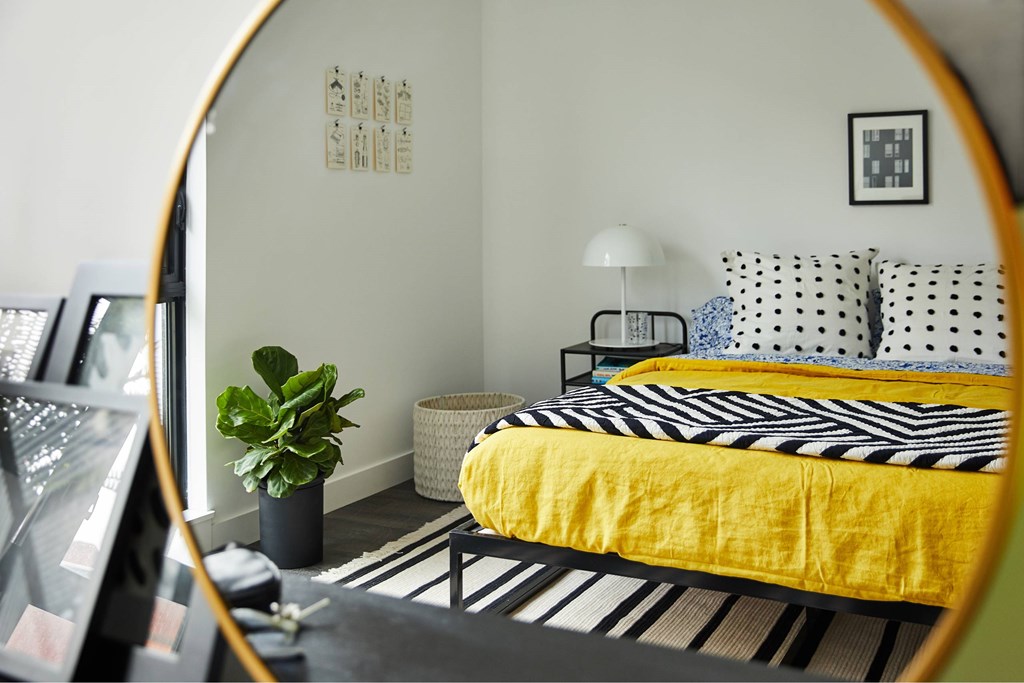 A bedroom with a yellow bedspread and a black and white striped rug.