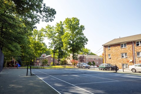 A tennis court surrounded by trees and a brick building.