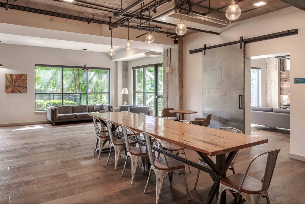 A long wooden table is surrounded by chairs in a room with a glass wall.
