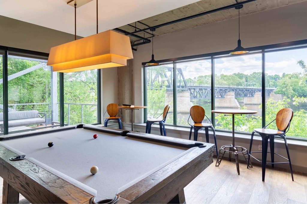 A pool table is in the middle of a room with a view of a bridge outside the window.